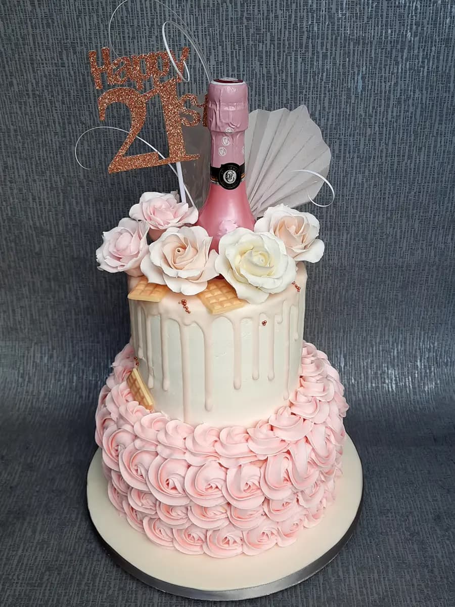 Two-tier 21st birthday cake with pink rosettes, white drip, and champagne decoration