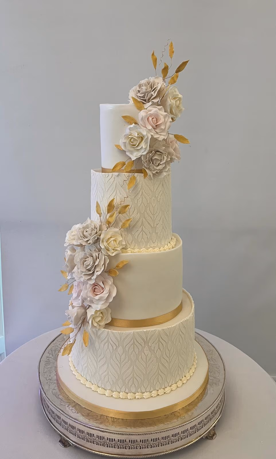 Four-tier cream and gold textured wedding cake with roses