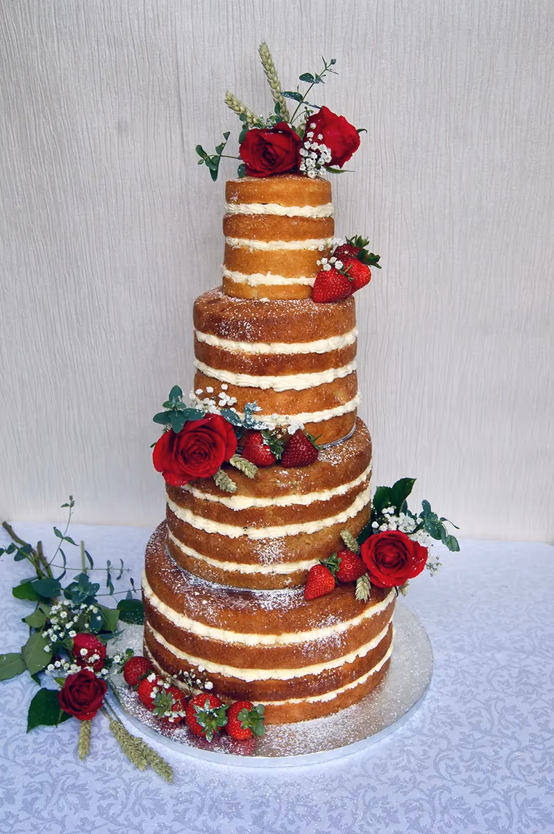 Six-tier naked wedding cake with red roses, strawberries, and wheat