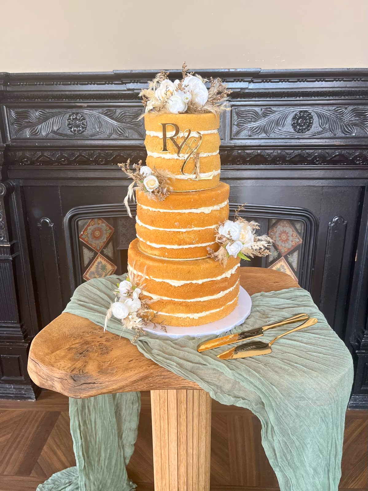 Three-tier naked wedding cake with white and dried flowers and a gold monogram topper