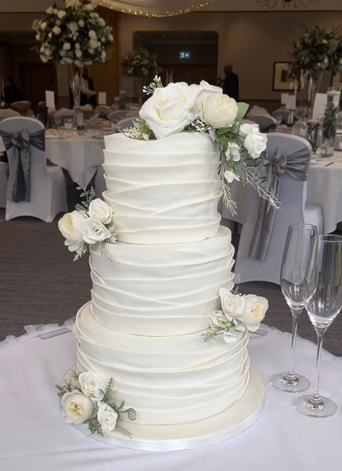 Three-tier white ruffled fondant wedding cake with ivory roses
