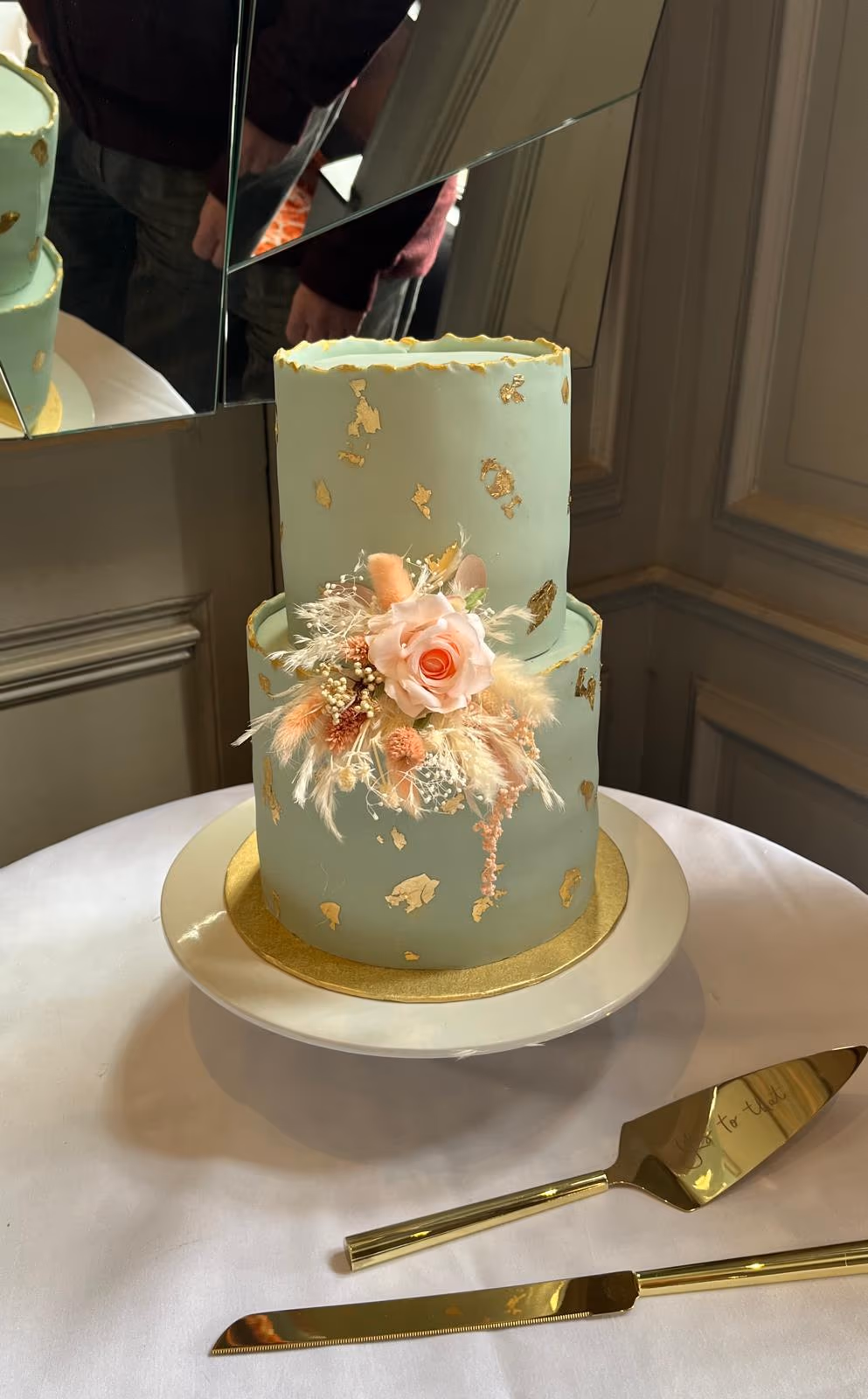 Two-tier sage green wedding cake with gold leaf and dried floral decoration